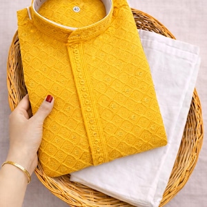 K&ouml;nnte beinhalten: Ein senfgelbes, besticktes Kurta-Set mit Stehkragen, kombiniert mit einer wei&szlig;en Hose, pr&auml;sentiert in einem Weidenkorb. Das Kurta hat aufwendige Diamantmuster und dekorative Details.