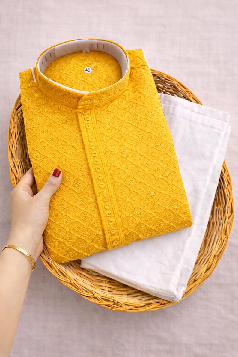 K&ouml;nnte beinhalten: Ein senfgelbes, besticktes Kurta-Set mit Stehkragen, kombiniert mit einer wei&szlig;en Hose, pr&auml;sentiert in einem Weidenkorb. Das Kurta hat aufwendige Diamantmuster und dekorative Details.