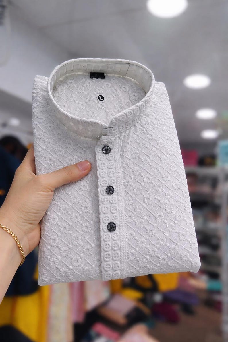 Woman holding a folded embroidered men’s kurta with mandarin collar and textured floral design, displayed in store.
