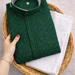 K&ouml;nnte beinhalten: Ein dunkelgr&uuml;nes, besticktes Kurta mit wei&szlig;em Kragen und einer passenden wei&szlig;en Hose, pr&auml;sentiert in einem Weidenkorb. Das Kurta weist aufwendige Details und eine Knopfleiste auf. Das Gr&ouml;&szlig;enetikett lautet 40.
