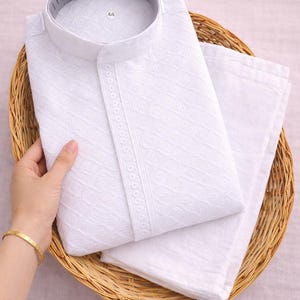 K&ouml;nnte beinhalten: Wei&szlig;es besticktes Kurta-Pyjama-Set, gefaltet in einem Weidenkorb. Das Kurta hat einen Stehkragen und aufwendige geometrische Muster. Das Set enth&auml;lt einen passenden Pyjama. Das Gr&ouml;&szlig;enetikett lautet "44".
