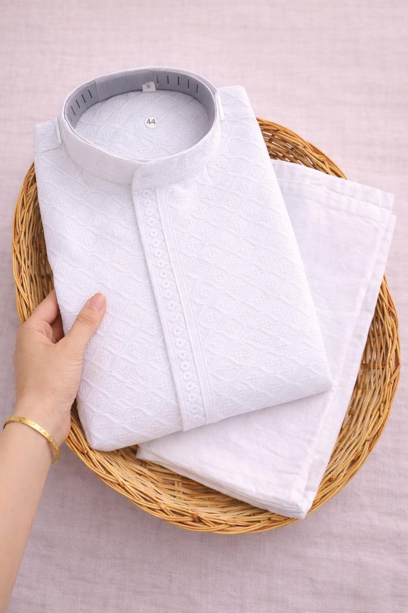 K&ouml;nnte beinhalten: Wei&szlig;es besticktes Kurta-Pyjama-Set, gefaltet in einem Weidenkorb. Das Kurta hat einen Stehkragen und aufwendige geometrische Muster. Das Set enth&auml;lt einen passenden Pyjama. Das Gr&ouml;&szlig;enetikett lautet "44".