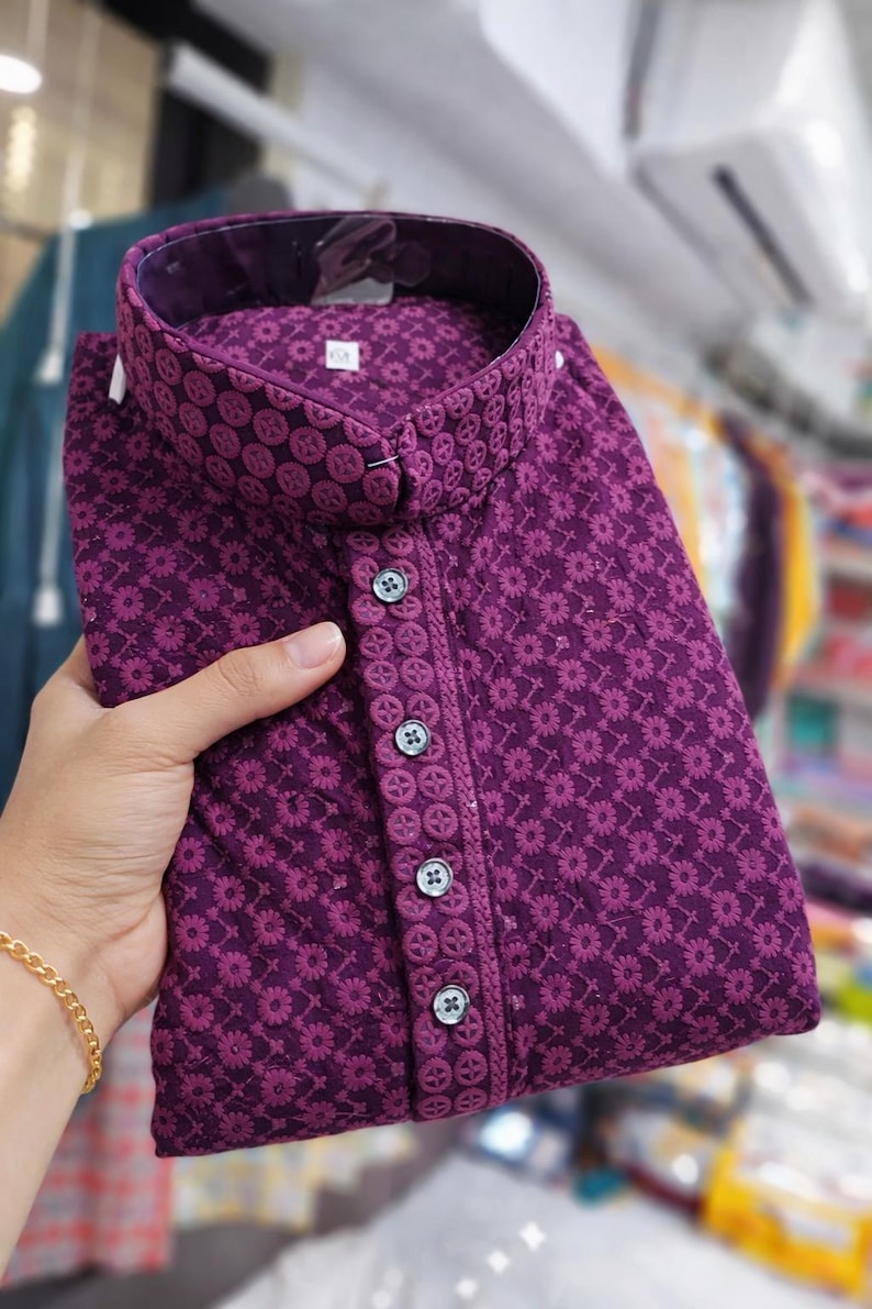 Woman holding a folded embroidered men’s kurta with mandarin collar and textured floral design, displayed in store.