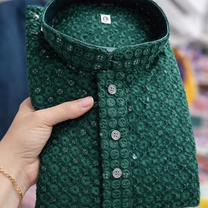 Woman holding a folded embroidered men’s kurta with mandarin collar and textured floral design, displayed in store.