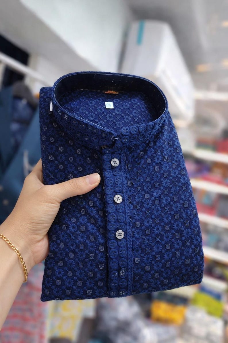 Woman holding a folded embroidered men’s kurta with mandarin collar and textured floral design, displayed in store.