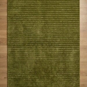 May include: A rectangular green rug with horizontal white stripes. The rug has a soft, textured appearance and is placed on a wooden floor. The rug's color is a vibrant shade of green, and the white stripes add a contrasting element to the design.