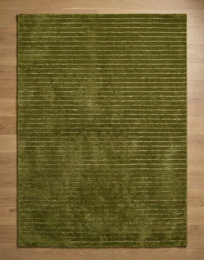 May include: A rectangular green rug with horizontal white stripes. The rug has a soft, textured appearance and is placed on a wooden floor. The rug's color is a vibrant shade of green, and the white stripes add a contrasting element to the design.