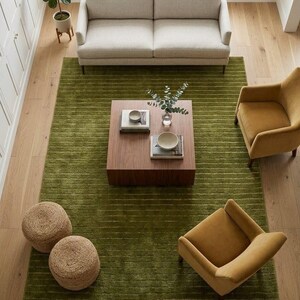 May include: An overhead shot of a living room with a light-colored sofa, two mustard-yellow armchairs, and a square wooden coffee table on a green rug. Two woven poufs and a potted plant are also visible.