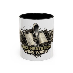 May include: White ceramic mug with a black interior, featuring a graphic design. The design includes an open book with wings, a stylized pen, and the text "DOCUMENTATION WINS WARS". The design has a grunge effect, with a bold font.