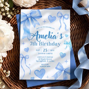 Può includere: Un biglietto d'invito di compleanno rettangolare bianco con fiocchi, cuori e stelle ad acquerello azzurro. Il testo recita: Join us to celebrate Amelia's 7th Birthday, Sat 25 Aug, 2:00PM-5:00PM, Amelia's House, 18 Maple Street, Springfield, IL 62704, RSVP by (651)555-0199.