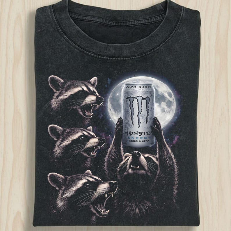 May include: Black t-shirt featuring a graphic of raccoons worshipping a Monster Energy Zero Ultra can in front of a full moon. The shirt has a vintage, distressed look.