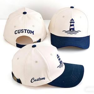 May include: Cream-coloured baseball cap with a navy blue brim and a navy blue lighthouse design. The word "CUSTOM" is embroidered on the back of the cap. The cap has a curved brim and an adjustable strap.