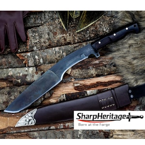 May include: A large, dark-bladed knife with a black handle and a brown leather sheath. The knife is displayed on a wooden surface with a fur-like texture. The sheath has decorative metal accents. The text "SharpHeritage" is visible.