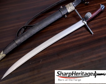 May include: A steel sword with a dark reddish-brown handle, a silver crossguard, and a ribbed pommel. The sword is accompanied by a black leather scabbard featuring ornate gold-colored metal fittings and a leather strap. Text reads SharpHeritage.