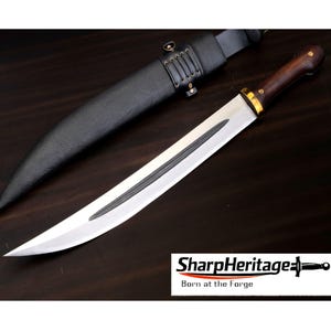 May include: A fixed-blade knife with a polished silver steel blade, a dark brown wooden handle with brass rivets, and a gold-coloured bolster. The knife is accompanied by a black leather sheath featuring a laced detail. Text reads SharpHeritage.
