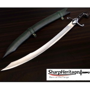 Puede incluir: Una espada de acero curva con mango oscuro y guarda plateada, acompañada de una vaina verde oscuro texturizada. La imagen incluye el texto SharpHeritage Born at the Forge con un pequeño icono de espada en la esquina inferior derecha.