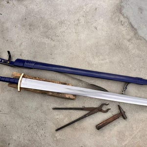 May include: A double-edged steel sword with a blue leather-wrapped grip, a gold-colored pommel and crossguard, and a matching blue leather scabbard with gold-colored metal fittings. A pair of iron blacksmith tongs and a small hammer are included.