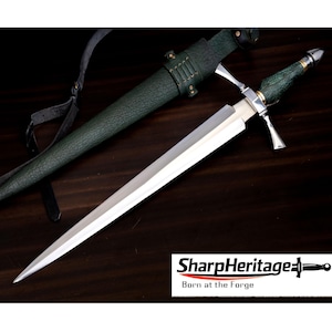 Puede incluir: Una daga de tono plateado con hoja de doble filo, guarda transversal y mango verde texturizado. Se acompaña de una funda verde texturizada a juego con una correa negra. El texto SharpHeritage Born at the Forge es visible.
