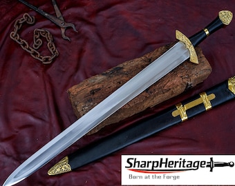 Puede incluir: Una espada de acero con mango negro y detalles de metal dorado en el pomo y la guarda. La espada presenta una hoja de doble filo y viene con una vaina negra que tiene herrajes de metal dorado en la punta y en la parte central.