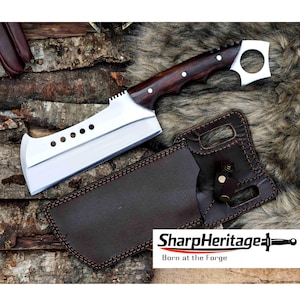 May include: A large, stainless steel cleaver with a dark wood handle and a leather sheath. The cleaver has a series of holes along the blade and a unique, squared-off design. The sheath is brown with decorative stitching.