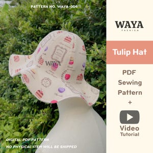 May include: A cream-colored tulip hat with a repeating pattern of cakes, macarons, and French text. The hat has a wide brim and is displayed on a mannequin head. The image also includes the text "Tulip Hat" and "PDF Sewing Pattern + Video Tutorial."