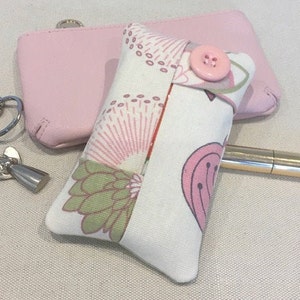 Peut inclure: Un petit porte-mouchoirs en tissu à motif floral rose et vert avec une fermeture à bouton rose. Le porte-mouchoirs est posé sur une surface beige clair.