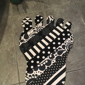 May include: A black and white foot-shaped rug with various patterns, including polka dots, stripes, and floral designs. The rug is made of fabric and is designed to be placed on the floor. The rug is a decorative item.