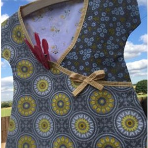 May include: A gray and yellow fabric laundry bag with a floral print and a bow. The bag is hanging on a wooden hanger and has a pocket on the front.