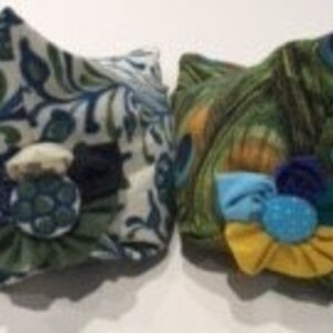 May include: Two fabric face masks with floral patterns. One mask is green and white with a blue button, the other is green with blue, yellow, and white fabric accents.