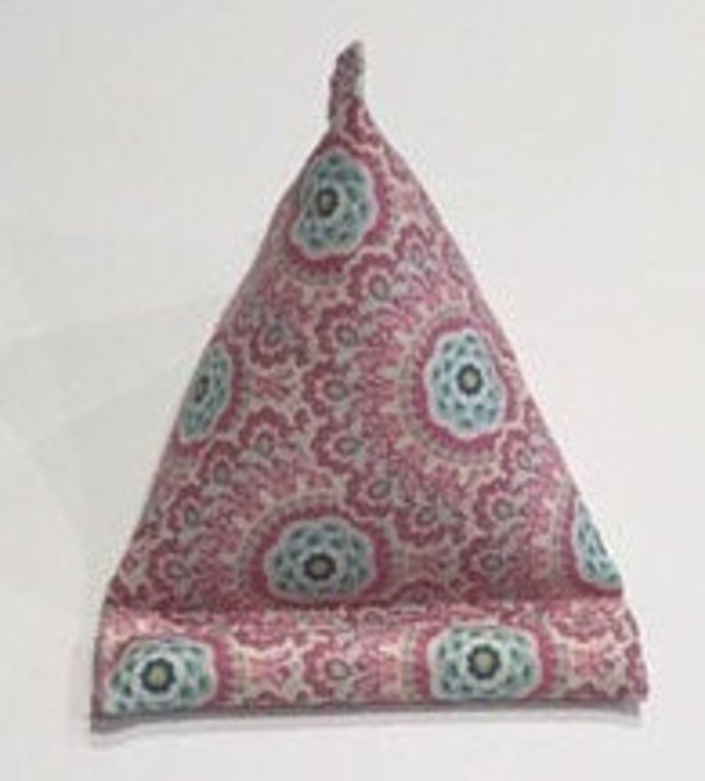 May include: A pink and blue patterned triangular pillow with a decorative design. The pillow is filled with stuffing and can be used to prop up a book or tablet.