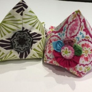 May include: Two fabric bookends, one with a green and brown floral pattern and the other with a pink and white floral pattern. Both bookends have a triangular shape and are decorated with a flower.