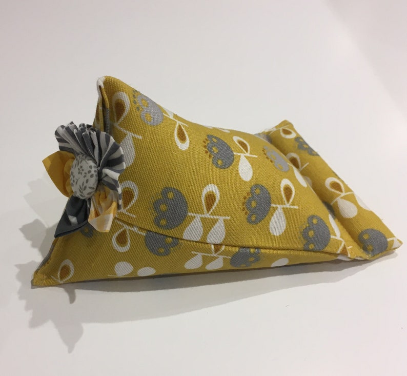 May include: A yellow and gray fabric wedge pillow with a floral design. The pillow has a gray and white flower sewn on the front.