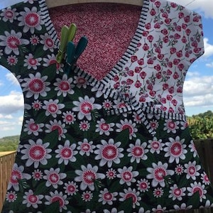 May include: A black and white floral print fabric with a pink and white floral print fabric on the top. The fabric is hanging on a wooden hanger. There are three clothes pegs on the fabric.