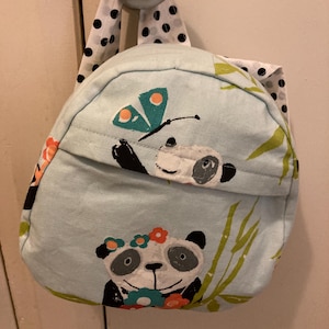 May include: A light blue backpack with a panda and butterfly design. The backpack has a black and white polka dot strap.