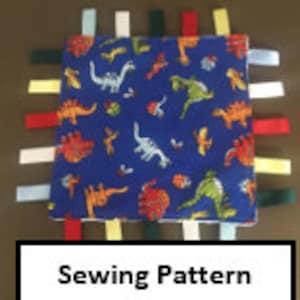 Puede incluir: Un cuadrado de tela azul con estampado de dinosaurios y lazos de cinta de colores. Este es un patrón de costura para un juguete sensorial para bebés o niños pequeños.