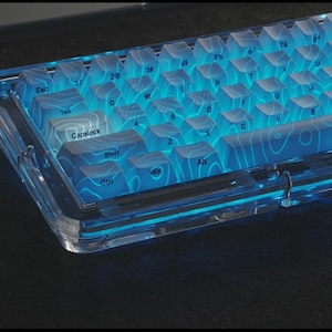 May include: A transparent mechanical keyboard with blue LED backlighting. The keycaps are clear with a topographic design, and the keyboard has a clear frame. The keys are labeled with white letters and symbols.