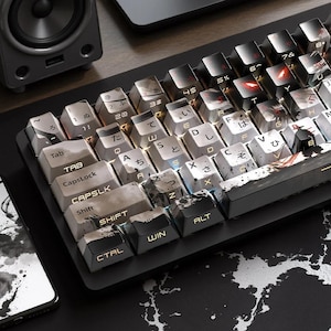 May include: A black mechanical keyboard with custom keycaps. The keycaps feature a mix of white, gray, and black colors with Japanese characters and abstract designs. The keyboard is on a black and white patterned surface.