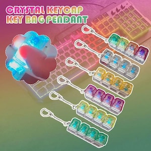 Peut inclure: Pendentifs de sac à clés en forme de touches de clavier en cristal de différentes couleurs, chacun avec un porte-clés argenté. Les pendentifs sont conçus pour ressembler à des touches de clavier et sont présentés sur un fond de clavier rétroéclairé. Le texte "CRYSTAL KEYCAP KEY BAG PENDANT" est en haut.