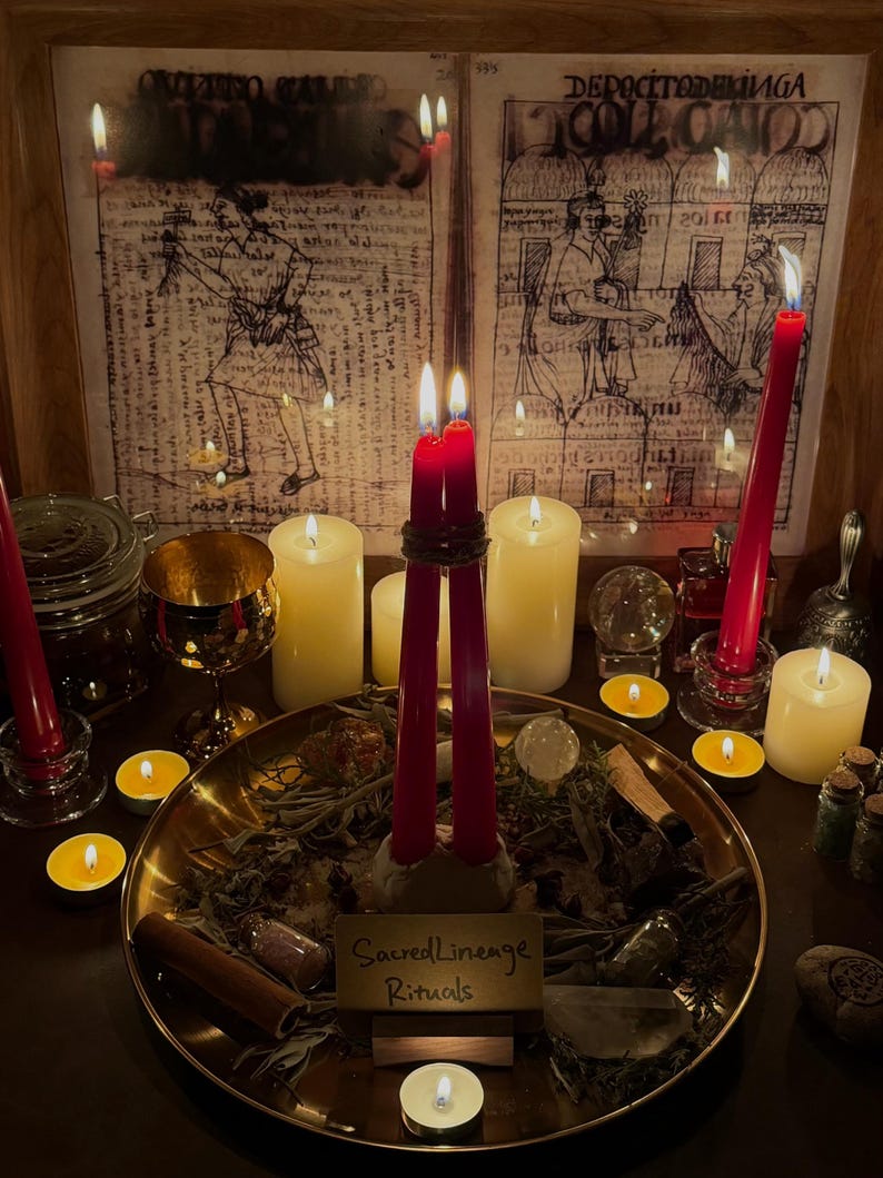 May include: A dimly lit scene featuring candles, a brass tray with herbs, and two framed illustrations. Tall red candles are lit, along with smaller tea lights. The brass tray has a sign that reads "Sacred Lineage Rituals".