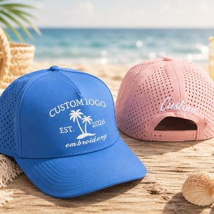 May include: A bright blue baseball cap with white embroidery featuring two palm trees and the text CUSTOM IOGO EST. 2026 embroidery, alongside a light pink perforated baseball cap with the word Custom embroidered in white on the back.