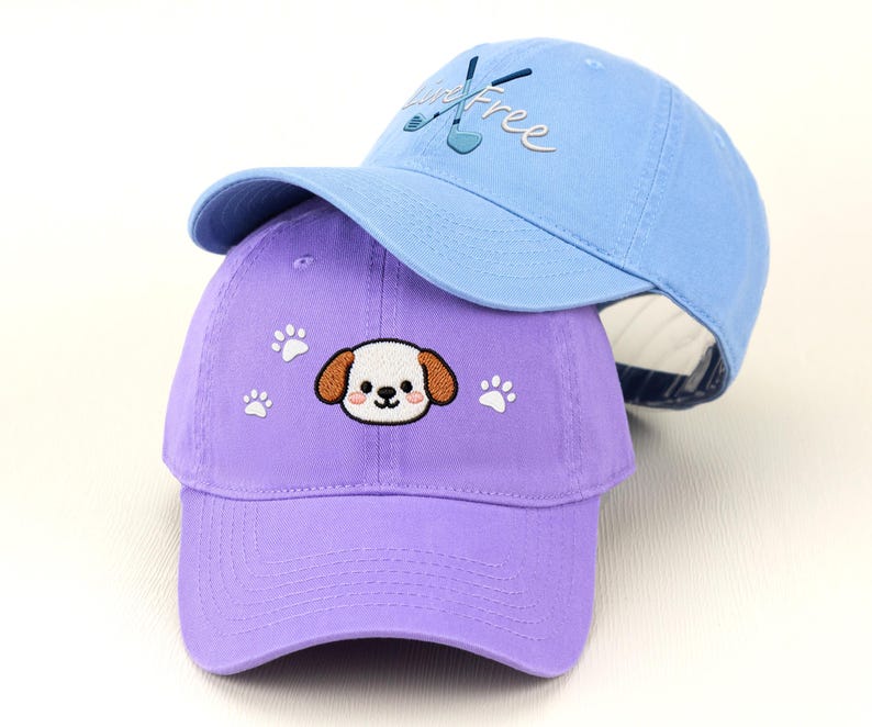 May include: Two baseball caps, one light blue and one purple. The light blue cap has the word "Free" embroidered on it, along with golf clubs. The purple cap features a puppy face and paw prints.