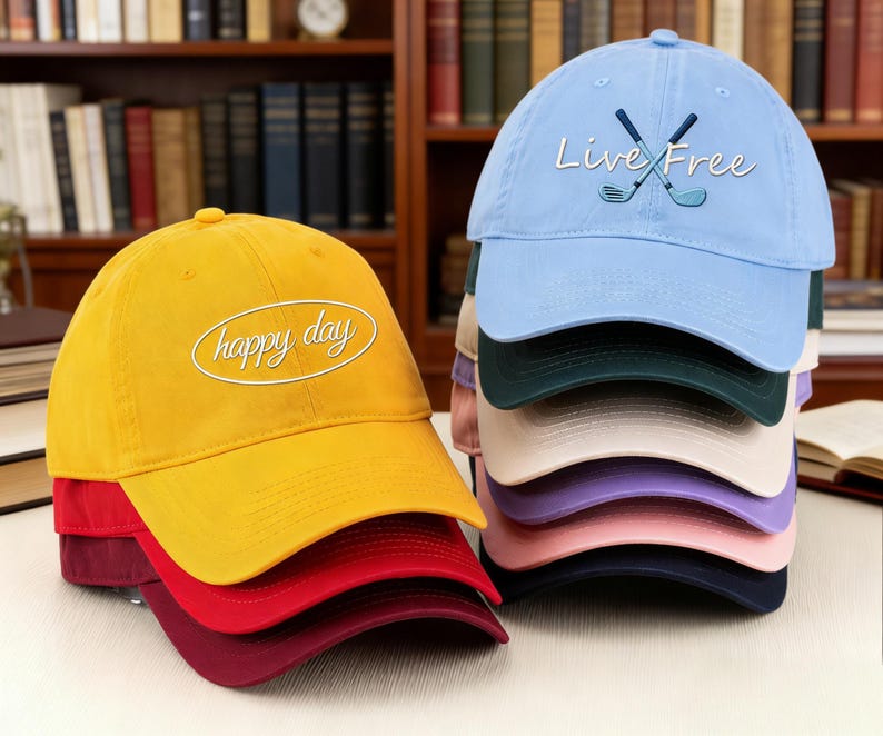 May include: A stack of baseball caps in various colors, including yellow, red, and blue. The yellow cap has the text "happy day" in white script. The blue cap features crossed golf clubs and the words "Live Free".