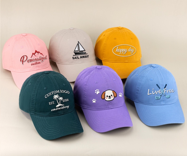 May include: A collection of six baseball caps in various colors, including pink, green, yellow, purple, and blue. Each cap features embroidered designs and text, such as a sailboat, a mountain, and the words "Happy Day" and "Live Free".