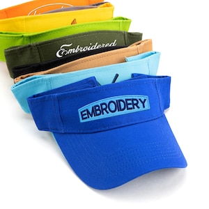 May include: A stack of colorful visors in shades of orange, yellow, green, brown, light blue, and blue. The blue visor has the word "EMBROIDERY" embroidered on the front. The green visor has the word "Embroidered" embroidered on the front.