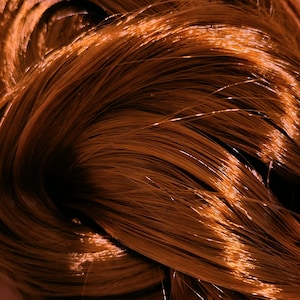 May include: A dense bundle of straight, glossy hair strands in a vibrant copper-orange hue. The fibers are arranged in a swirling, overlapping pattern, creating a smooth, reflective texture with deep shadows and bright highlights throughout the mass.