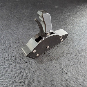 May include: A black 3D-printed gear shifter assembly featuring a vertical handle with a trigger mechanism. The base unit displays the letters D, N, and R in white, and the side panels are secured with four visible silver metal screws.