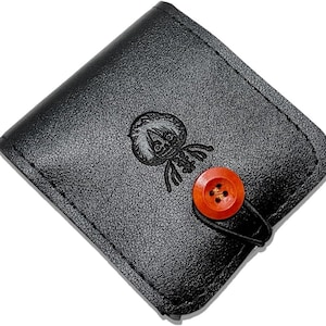 May include: Black leather wallet with a debossed cartoon character design. The wallet features a round, orange button closure and a black strap. The wallet is square-shaped and has a textured surface.