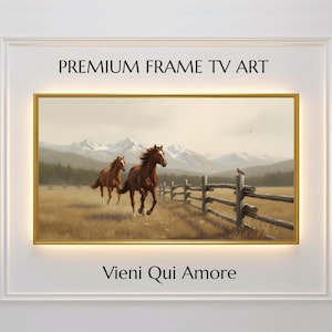 Puede incluir: Pintura de paisaje enmarcada con dos caballos marrones corriendo por un campo con una valla de madera. El fondo muestra montañas y un cielo nublado. Texto: "PREMIUM FRAME TV ART" y "Vieni Qui Amore".