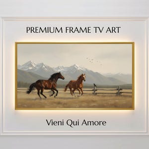 Puede incluir: Pintura de paisaje enmarcada con dos caballos corriendo por un campo. La obra de arte tiene un marco dorado y representa una cordillera en el fondo. Se muestra el texto "PREMIUM FRAME TV ART" y "Vieni Qui Amore".