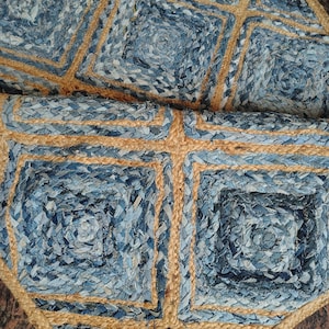 May include: Close-up of a blue and tan rug. The rug features a geometric pattern of squares and diamonds. The squares are made of blue denim material, and the diamonds are made of tan jute. The rug is a decorative home decor item.